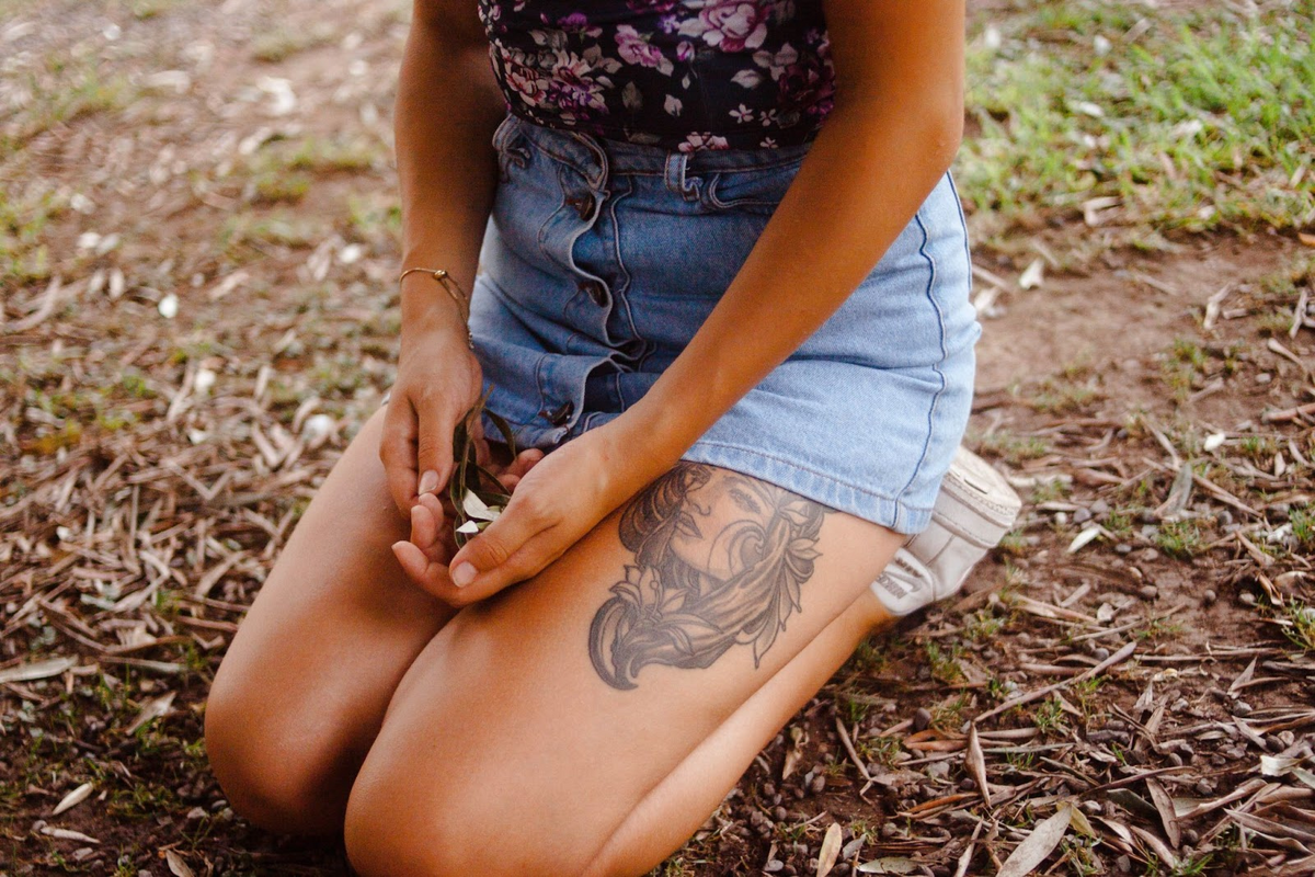 Tanned girl with face portrait tattoo on upper thigh