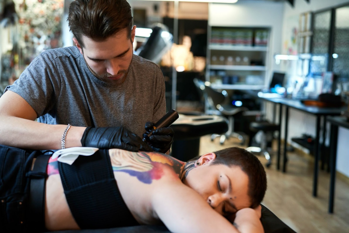 Caucasian man tattooing back of female customer in tattoo studio