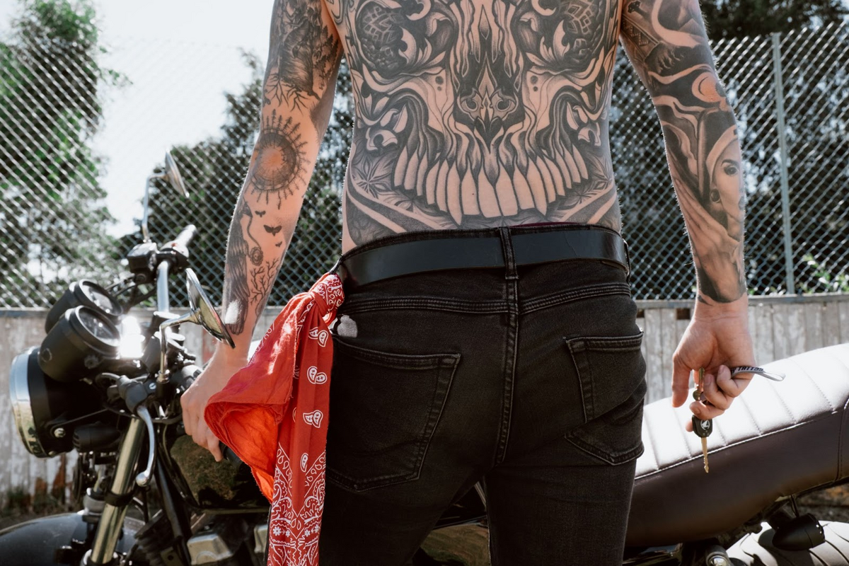 full back tattoo on man standing behind motorbike
