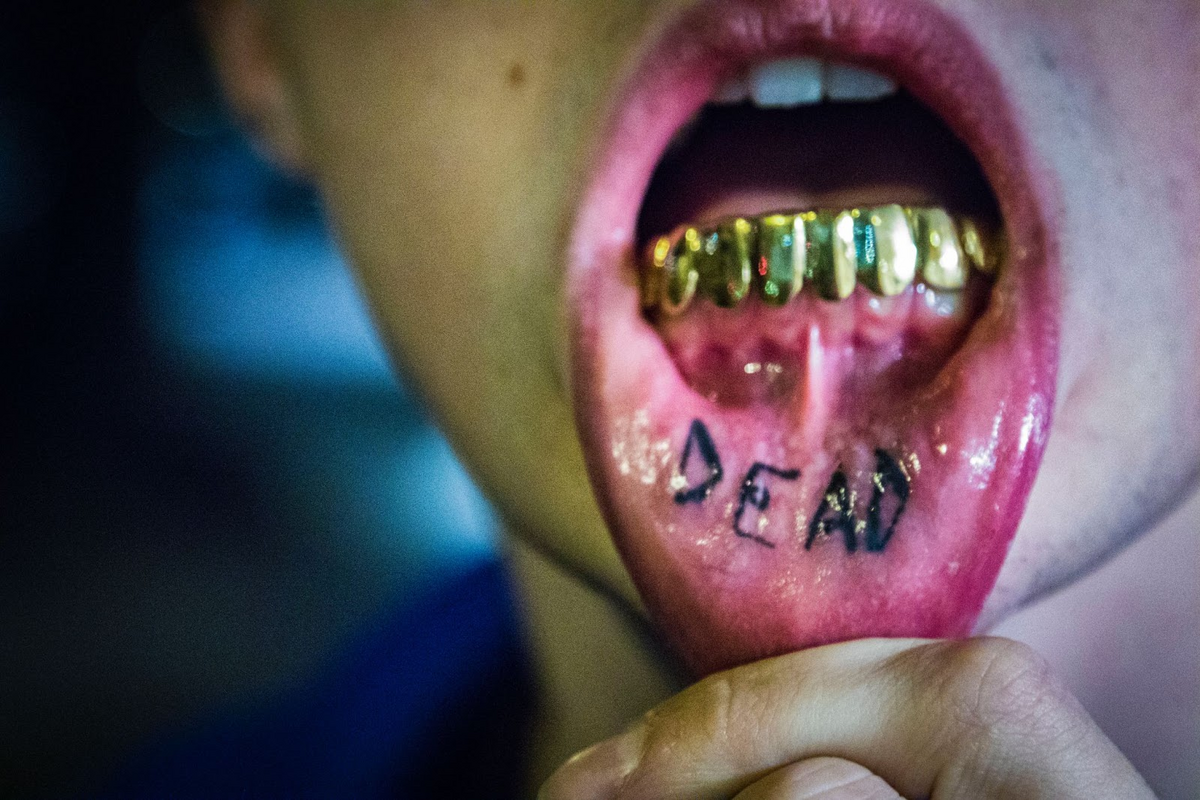 man with inner lip tattoo saying dead and gold teeth