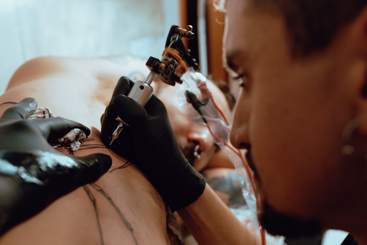 man getting tattoo on his rib cage with tattoo gun