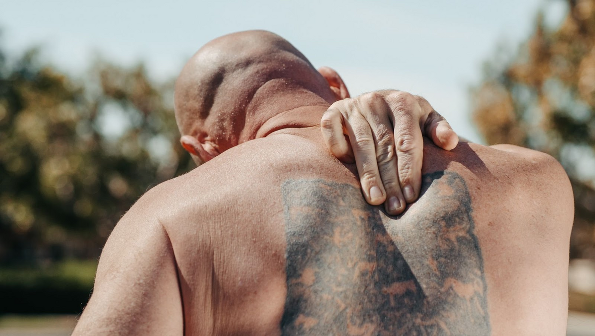 man reaching to his back to press his faded spine tattoo